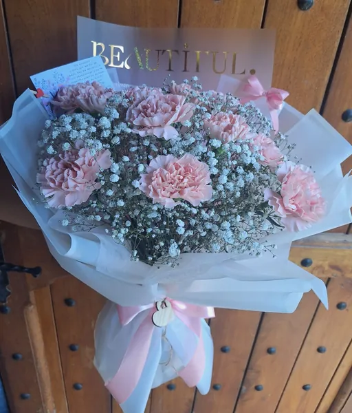 Ramo de claveles rosados con flor de novio en papel blanco